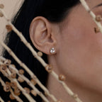 Close-up of a woman's ear wearing Oval Diamond Studs, with dried plant stems in the foreground.