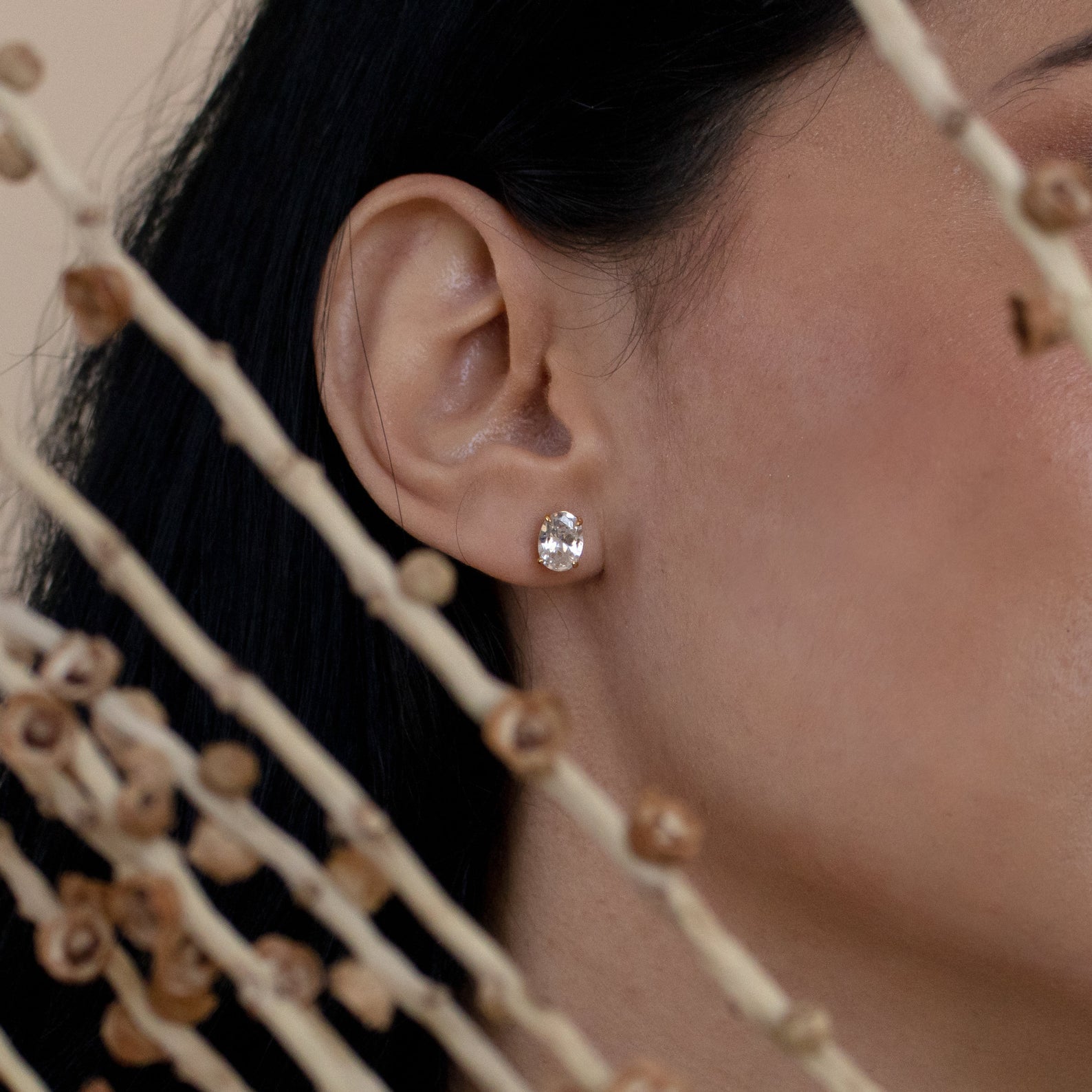Close-up of a woman's ear wearing Oval Diamond Studs, with dried plant stems in the foreground.