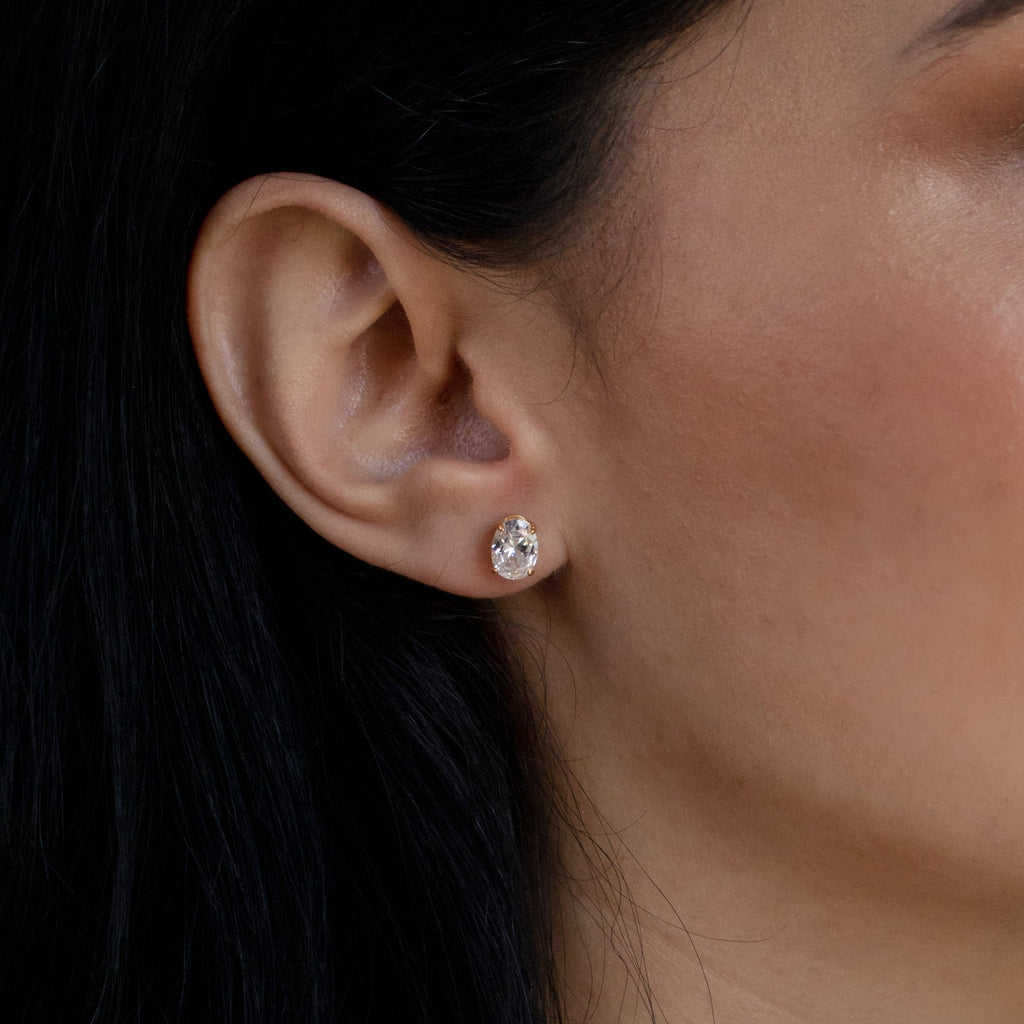 Close-up of a woman's ear wearing Oval Diamond Studs—classic jewelry with her dark hair tucked behind her ear.