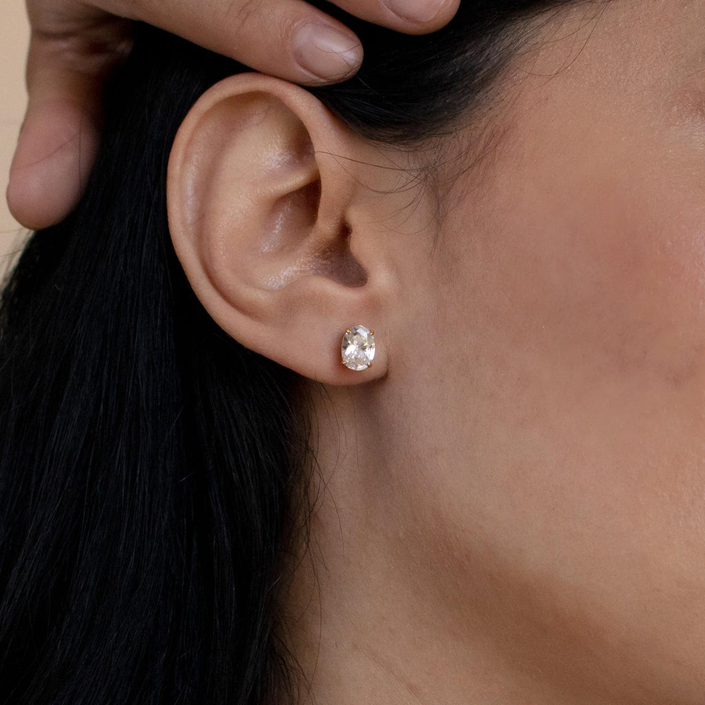 A close-up of a woman's ear adorned with Oval Diamond Studs as she rests her hand on her head—an elegant touch of classic jewelry.