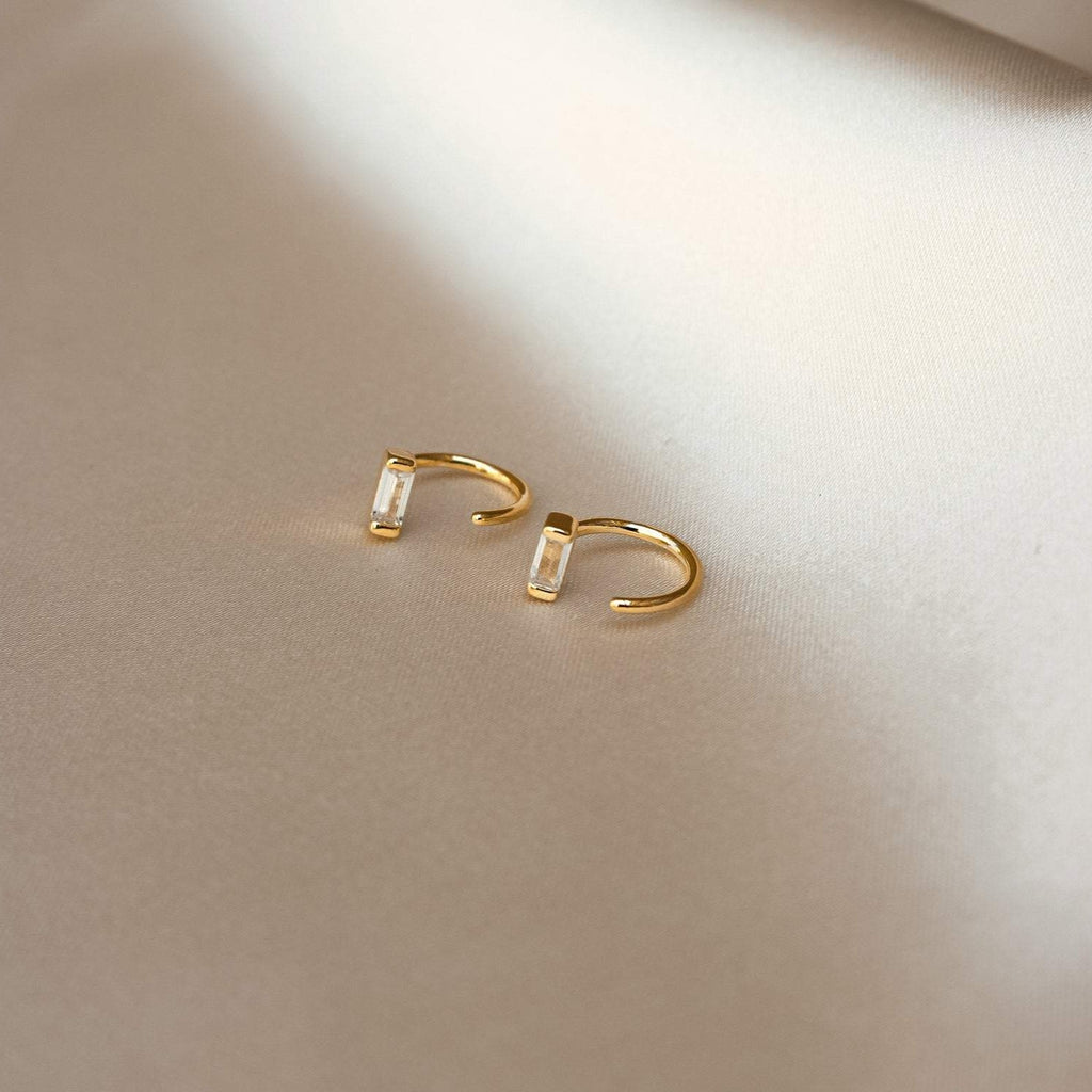 Shayla Baguette Huggies—gold open hoop earrings with baguette-shaped diamonds—displayed on a light, soft fabric surface.