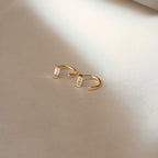 Shayla Baguette Huggies—gold open hoop earrings with baguette-shaped diamonds—displayed on a light, soft fabric surface.