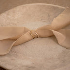 The Curve Stacking Set features two gold curved bands arranged on a beige fabric ribbon, displayed on a textured stone plate.