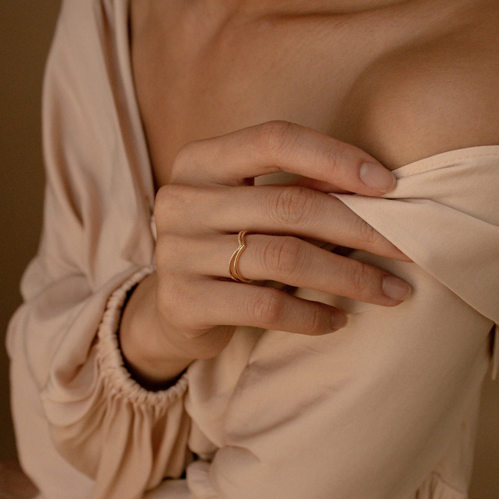 A person wearing the Curve Stacking Set, a gold curved band, touches their bare shoulder while dressed in a cream-colored off-shoulder blouse.