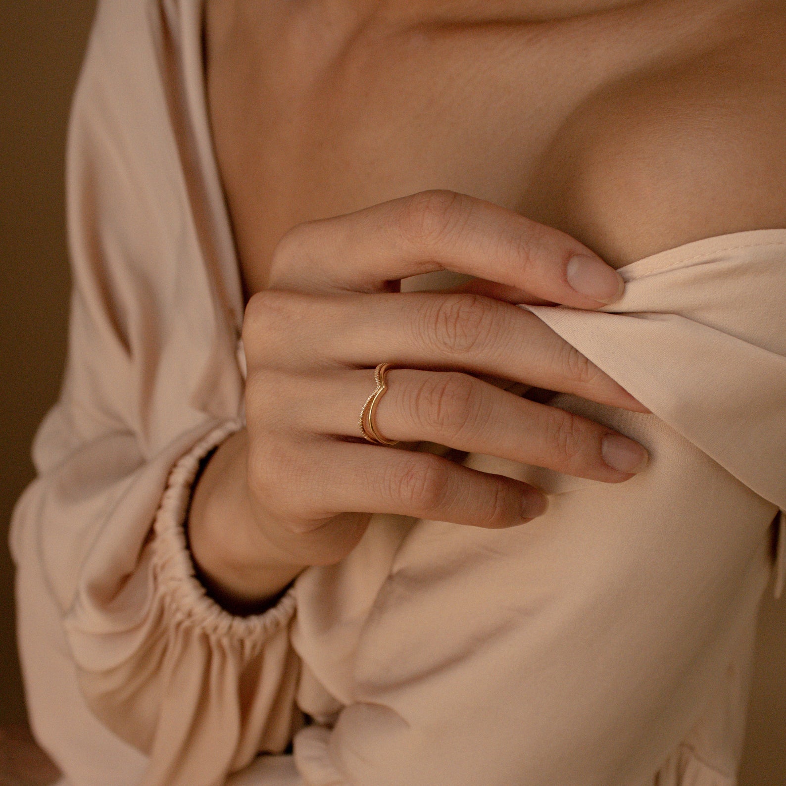A person wearing the Curve Stacking Set, a gold curved band, touches their bare shoulder while dressed in a cream-colored off-shoulder blouse.
