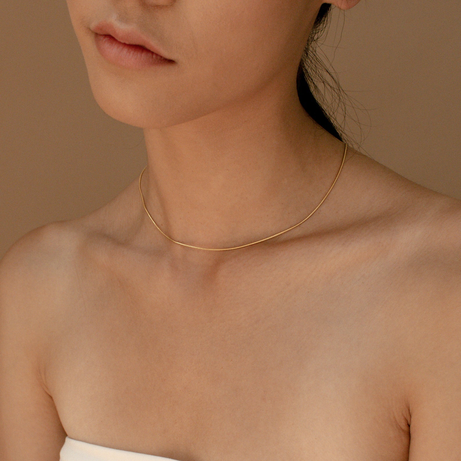 The gold snake chain necklace worn solo on a model, shown from the chest up with natural lighting