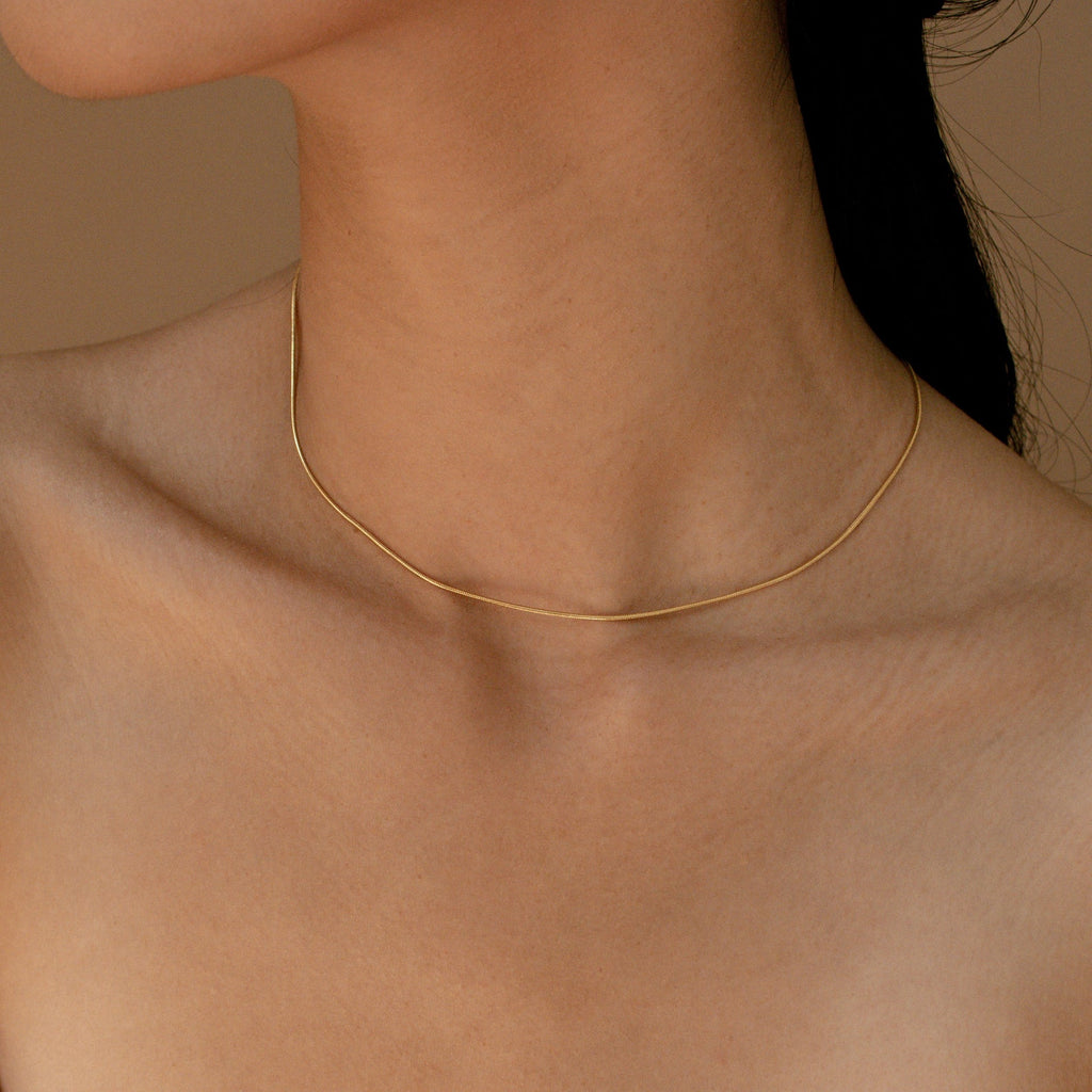 A minimal gold snake chain necklace worn close to the neck against bare skin