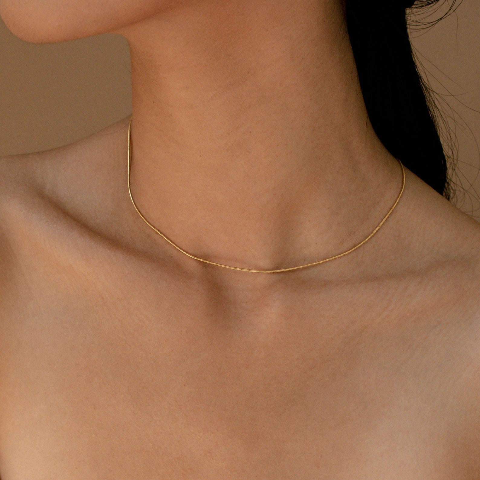 A minimal gold snake chain necklace worn close to the neck against bare skin