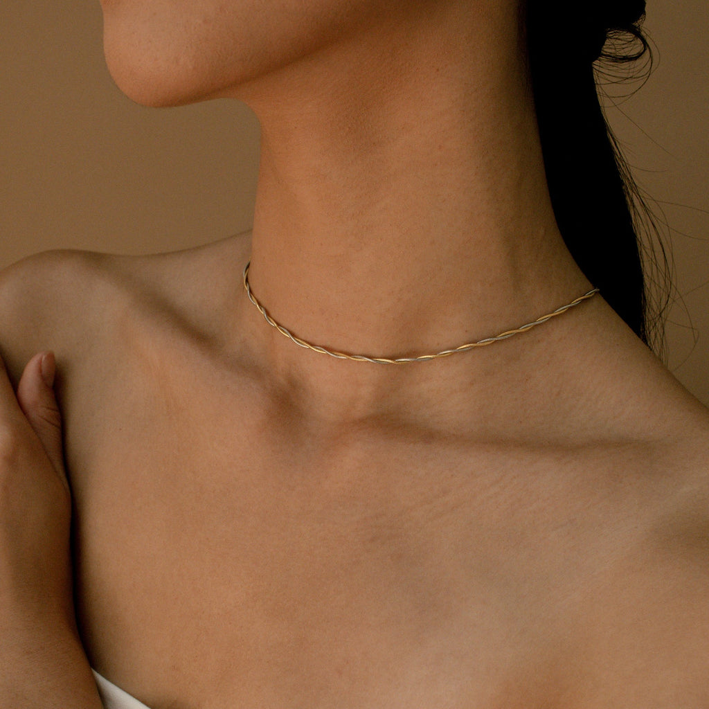 A twisted gold thin snake chain necklace styled tightly around the neck
