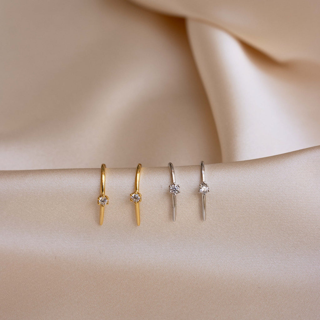 Two pairs of Rylee Diamond Wire Earrings in gold and silver are displayed on beige satin fabric, highlighting the modern elegance of these diamond earrings.