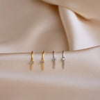 Two pairs of Rylee Diamond Wire Earrings in gold and silver are displayed on beige satin fabric, highlighting the modern elegance of these diamond earrings.