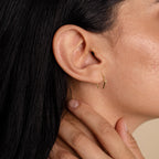 Close-up of a woman’s ear wearing the Rylee Diamond Wire Earrings, a delicate gold open hoop design, as her hand rests gently on her neck.