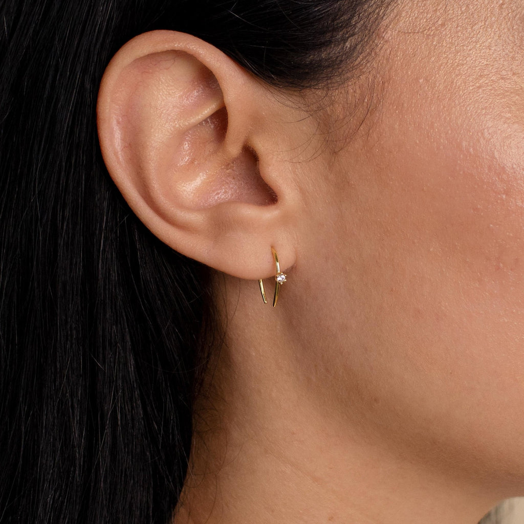Close-up of a woman's ear adorned with Rylee Diamond Wire Earrings, featuring a small, modern open hoop design accented by a single clear gemstone.