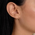 Close-up of a woman's ear adorned with Rylee Diamond Wire Earrings, featuring a small, modern open hoop design accented by a single clear gemstone.
