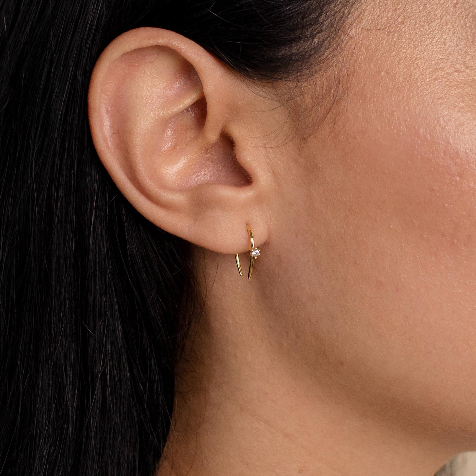 Close-up of a woman's ear adorned with Rylee Diamond Wire Earrings, featuring a small, modern open hoop design accented by a single clear gemstone.