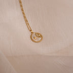 Gold celestial coin necklace with a round pendant featuring a crescent moon, star, and sunburst design, resting on a sheer beige fabric background.