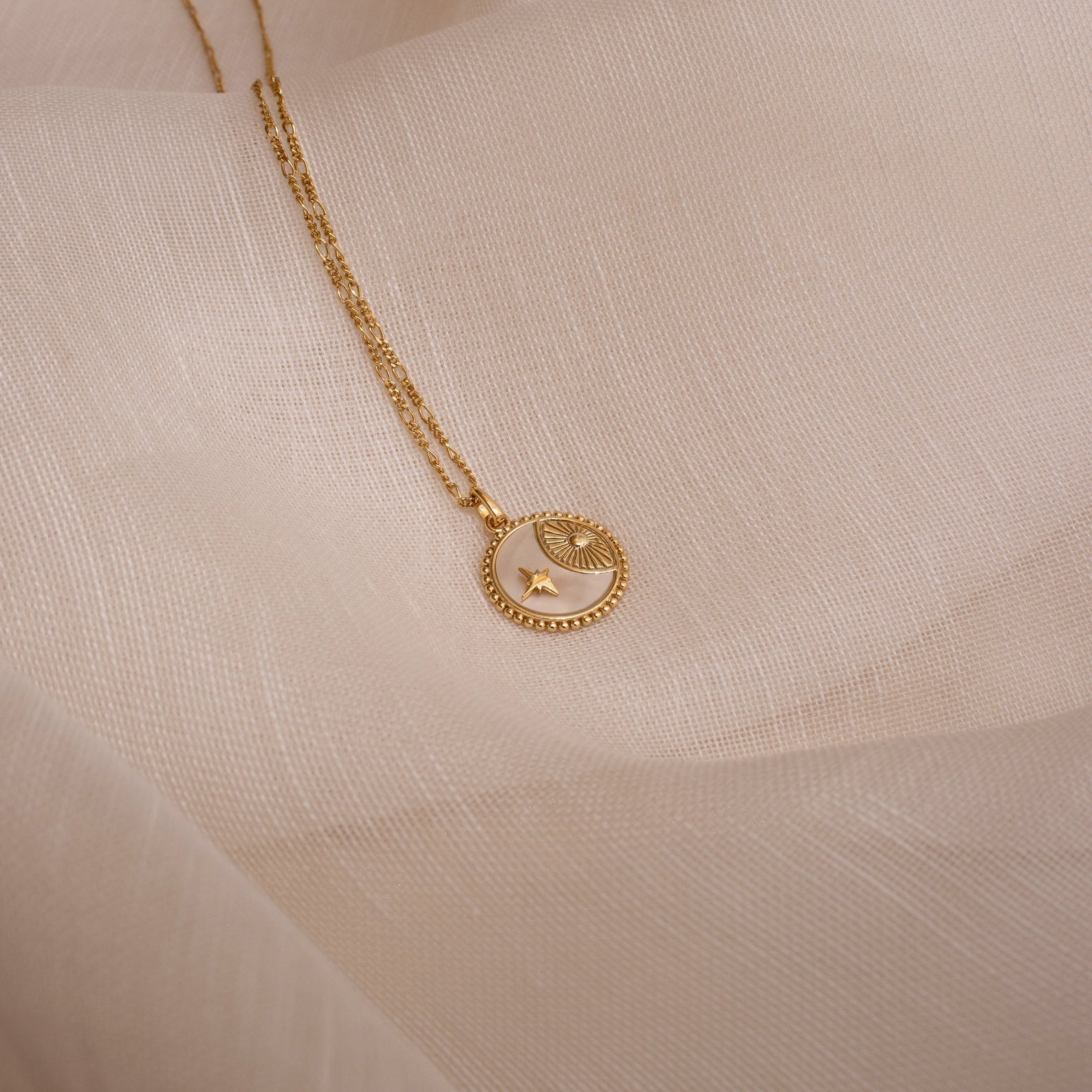 Gabi Coin Necklace with star and eye motifs, shown on soft beige fabric—a perfect minimalist accessory for jewelry lovers.