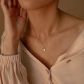 A person wearing a cream blouse with the Laura Starburst Duo Necklace in 18K Gold—featuring one diamond-accented chain and another with a star-shaped pendant.