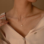 A woman in a light, off-shoulder blouse wears the Laura Starburst Duo Necklace in 18K Gold, featuring one diamond-accented chain and another with a star-shaped pendant.