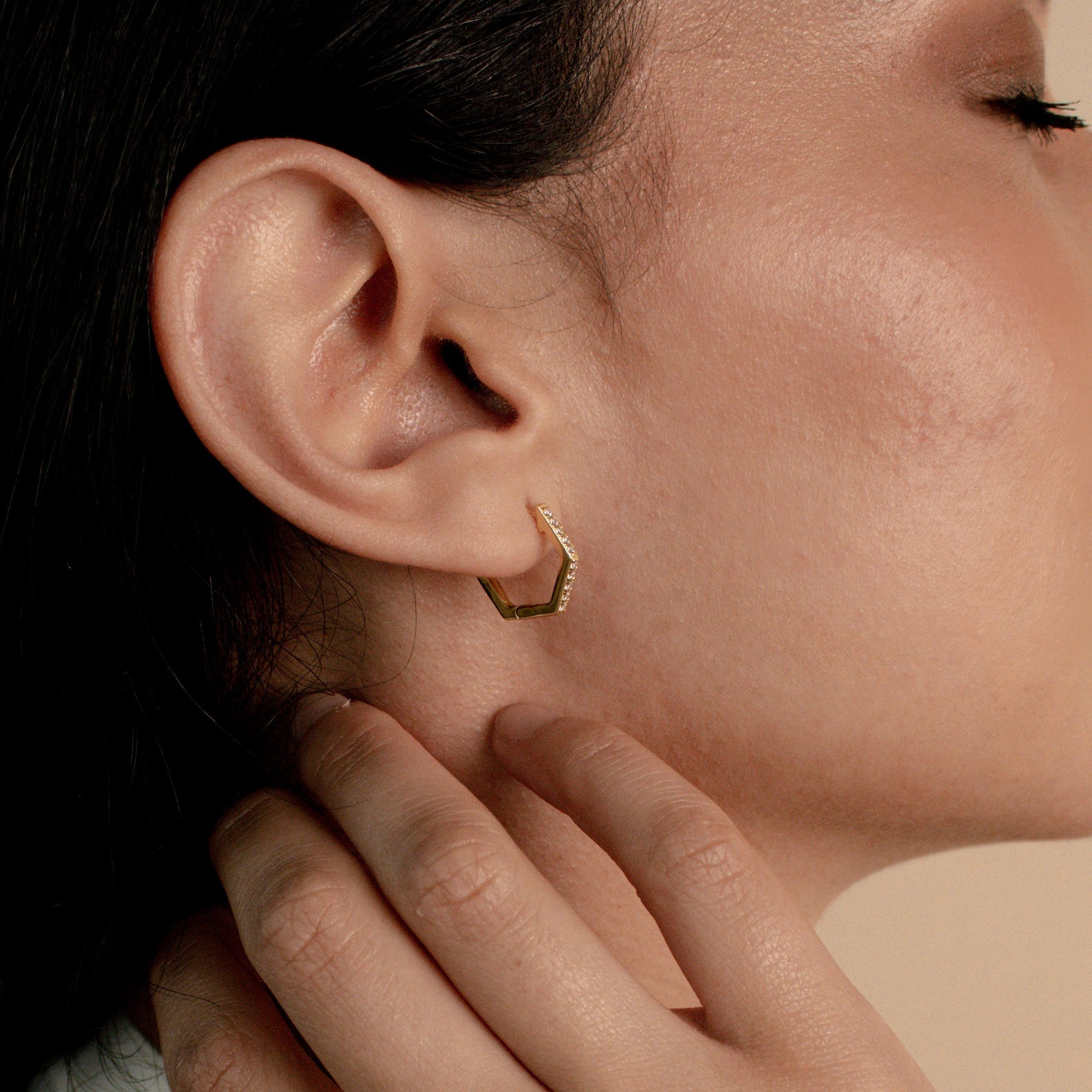 Close-up of a person wearing Parker Pave Hexagon Huggies, their hand gently touching their neck—an elegant ear adornment.