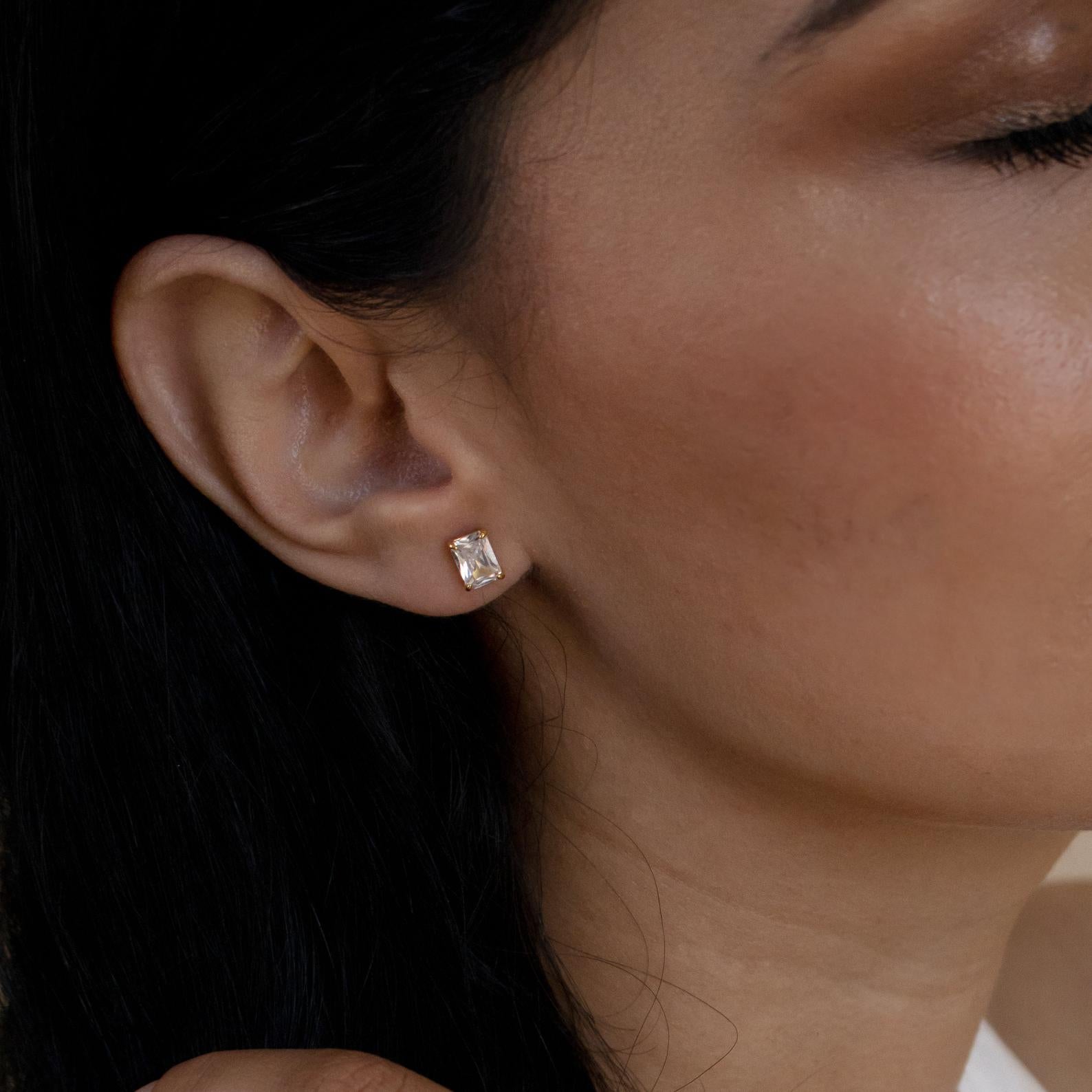 A close-up of a woman's ear wearing Emerald Diamond Studs with her eyes closed.
