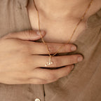 A hand holds the Initial Birthstone Necklace featuring a gold A pendant, styled over a beige shirt—a personalized gift ideal for any occasion.