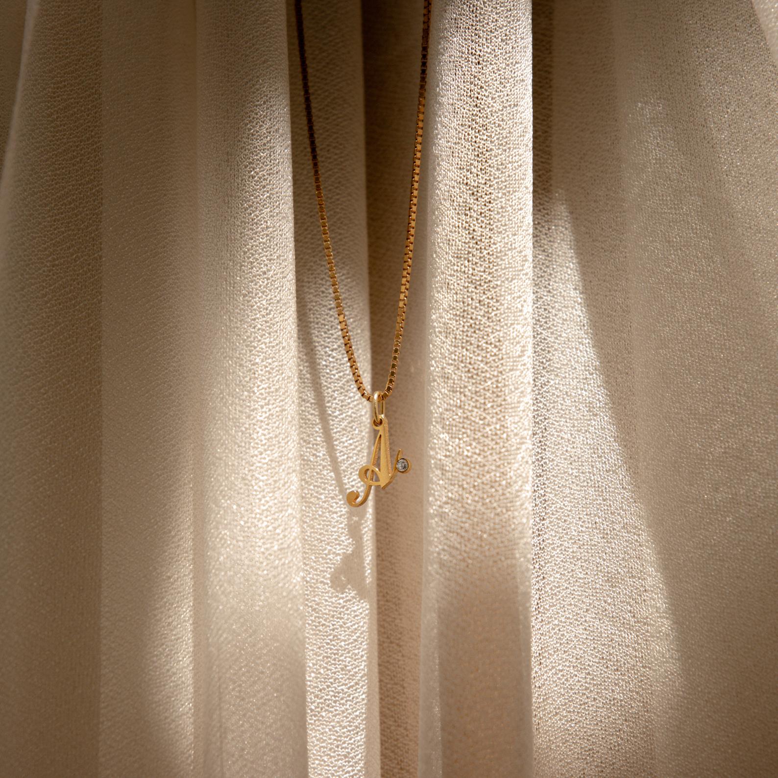 The Initial Birthstone Necklace pendant glows in sunlight against cream-colored curtains—a perfect personalized gift for any occasion.