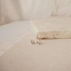 Pear Diamond Studs showcased on a light beige stone surface, these minimalist earrings stand out beautifully against a simple background.