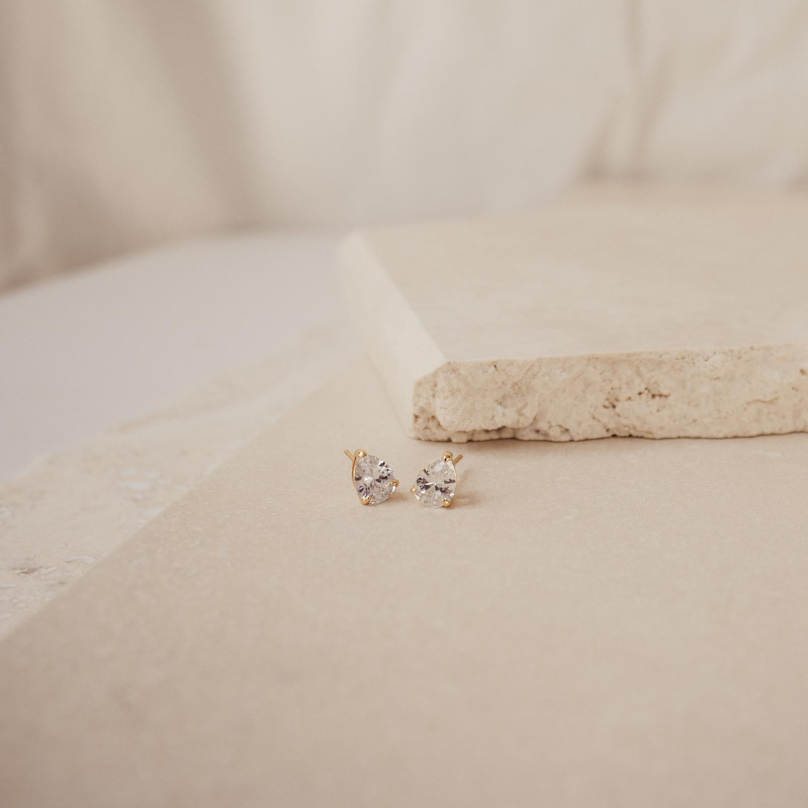 Pear Diamond Studs showcased on a light beige stone surface, these minimalist earrings stand out beautifully against a simple background.