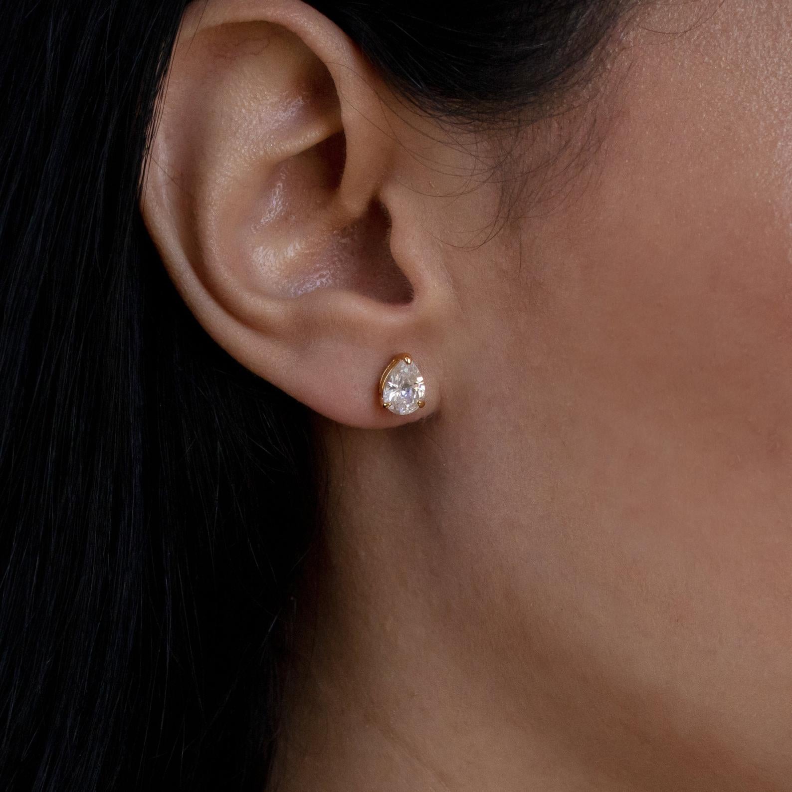Close-up of a woman's ear wearing Pear Diamond Studs: minimalistic gold earrings featuring a teardrop-shaped clear gemstone, ideal for everyday elegance.