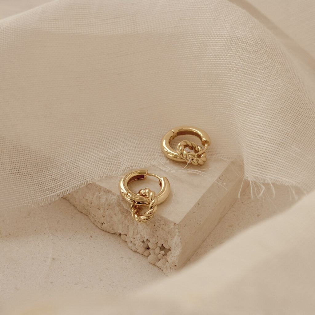 Claire Duo Hoops, displayed on textured stone with soft beige fabric, feature elegant rope detailing—chic earrings designed to effortlessly elevate any look.