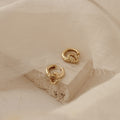 Claire Duo Hoops, displayed on textured stone with soft beige fabric, feature elegant rope detailing—chic earrings designed to effortlessly elevate any look.