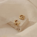 Claire Duo Hoops, displayed on textured stone with soft beige fabric, feature elegant rope detailing—chic earrings designed to effortlessly elevate any look.