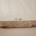 Classic Marquise Diamond Studs, featuring marquise-cut clear stones in a timeless gold setting, are elegantly displayed on a textured beige stone surface.
