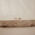 Classic Marquise Diamond Studs, featuring marquise-cut clear stones in a timeless gold setting, are elegantly displayed on a textured beige stone surface.