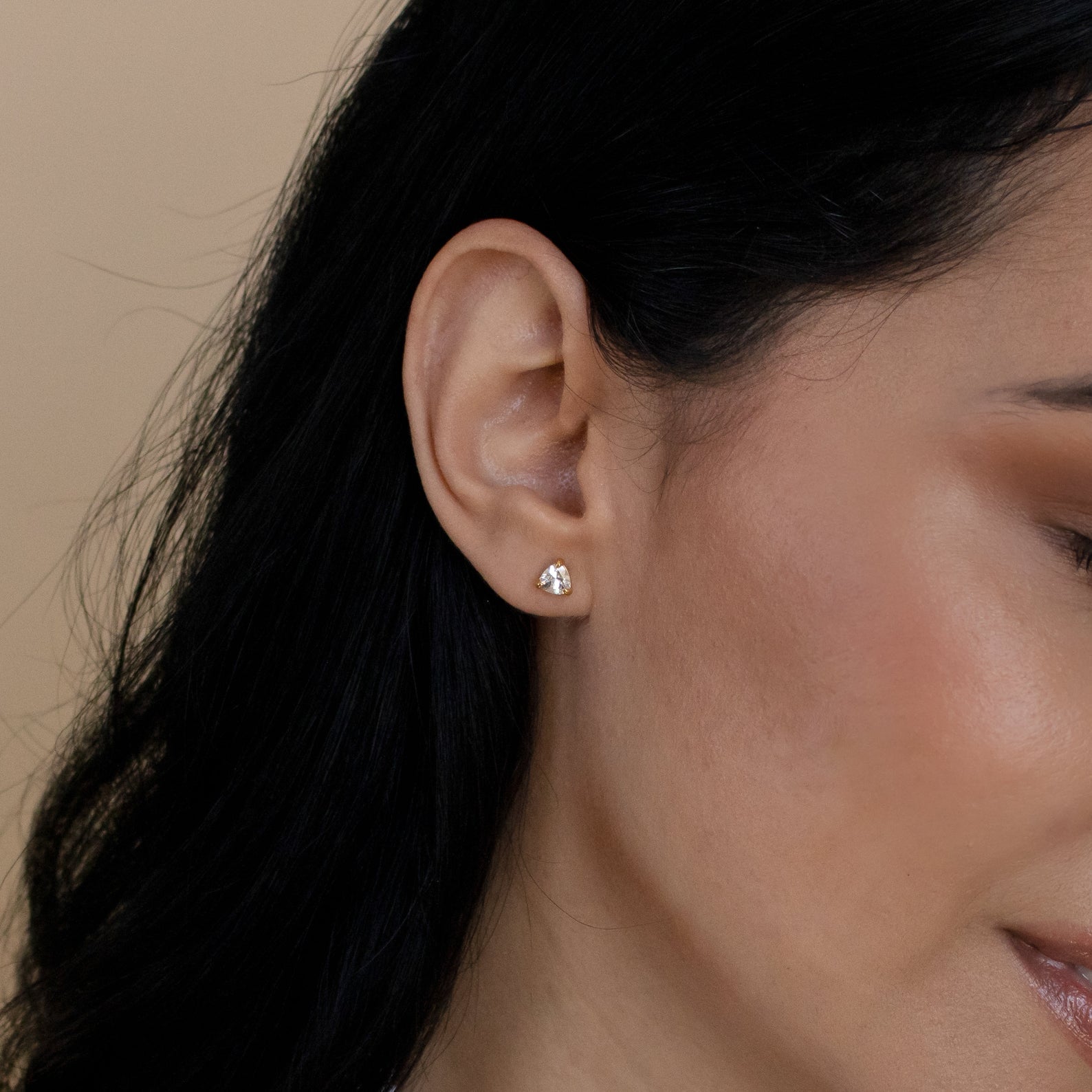 Close-up of a woman's ear adorned with Triangle Diamond Studs—an elegant, modern twist on classic jewelry—set against her dark hair.