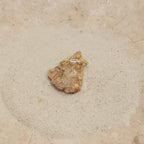 The Baguette Diamond Ring features a slim gold band and baguette diamonds, displayed on a small rock set on sand with a stone background.