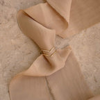 The Curve Stacking Set, featuring two gold and diamond chevron rings, is elegantly displayed on beige fabric atop a stone surface.