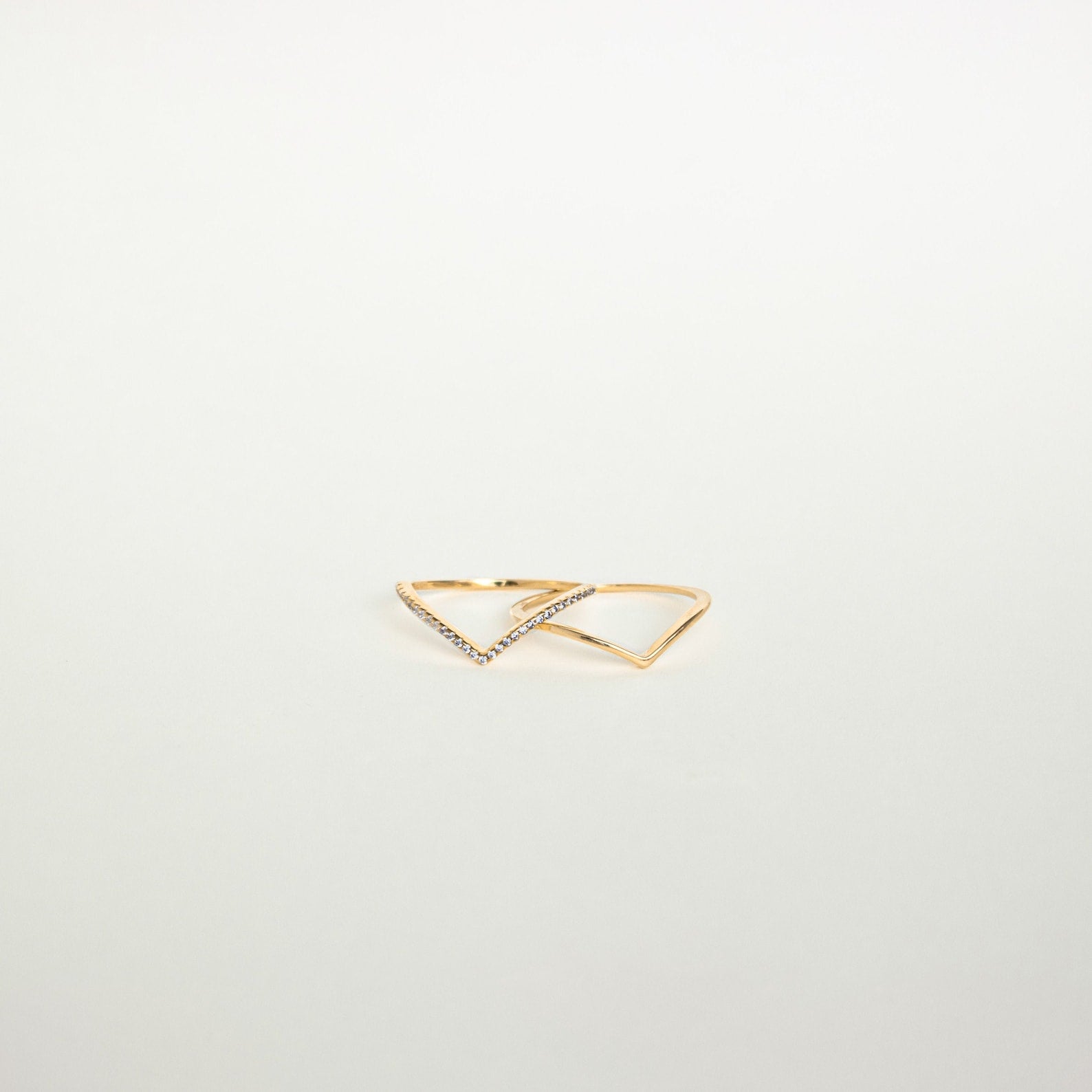 The Curve Stacking Set features two delicate gold rings with open triangle designs, one accented by small gemstones, offering a modern touch to your favorite ring stack.