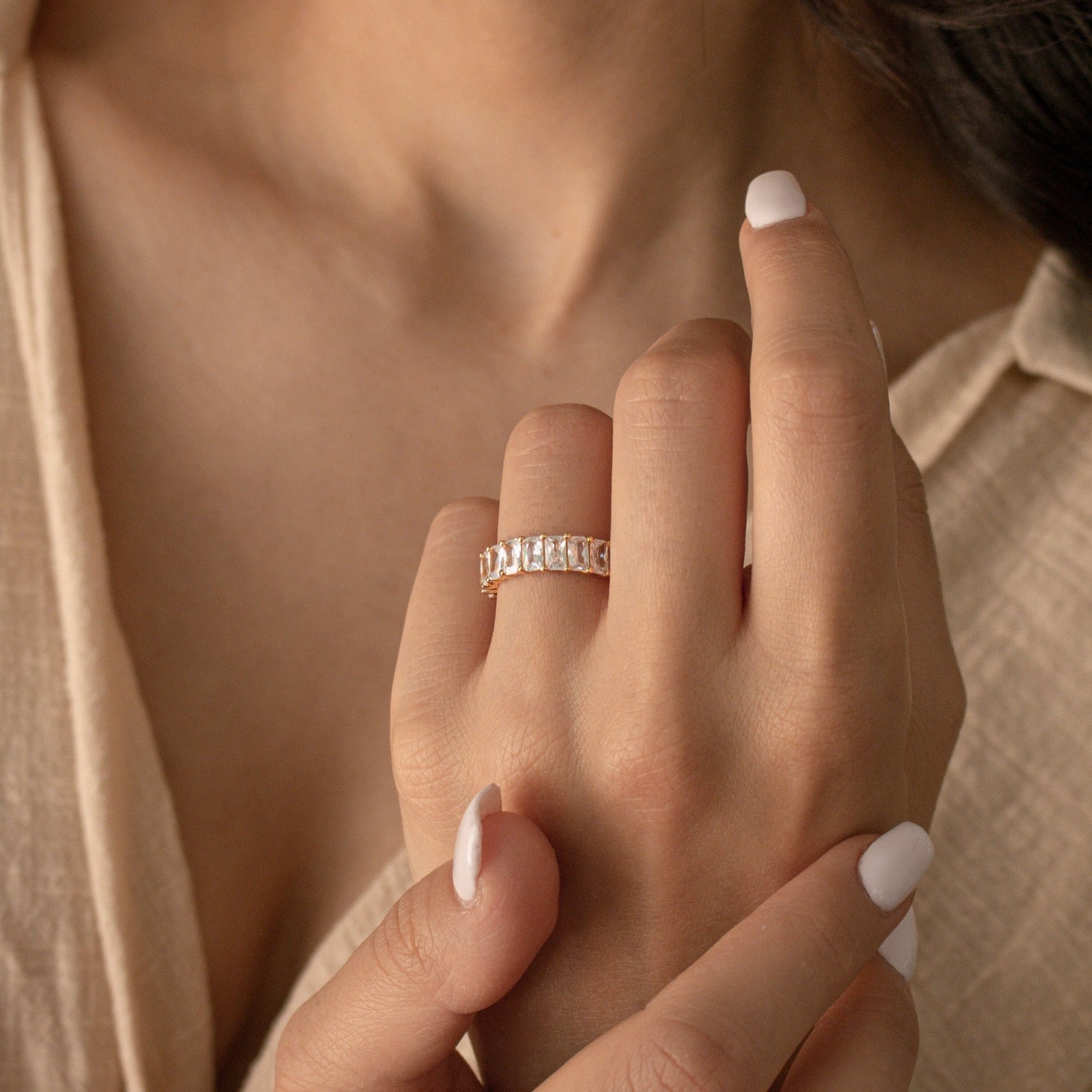 A woman with light nail polish wears the Colette Eternity Ring—a gold statement piece adorned with rectangular baguette diamonds—on her ring finger.