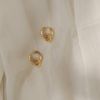 The Claire Duo Hoops are chunky earrings with elegant knot details, shown on sheer light beige fabric—ideal for fans of chic jewelry.