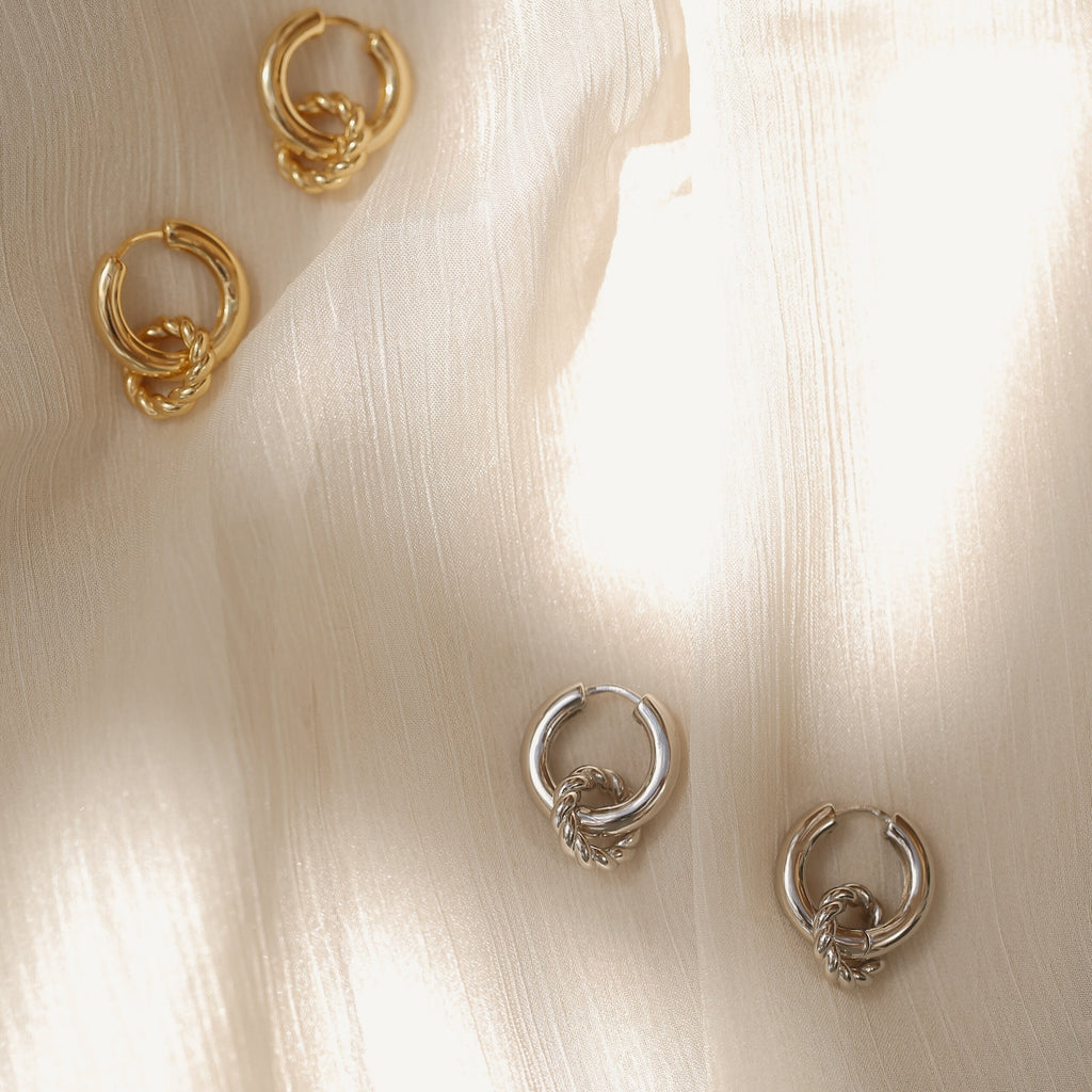 Two pairs of Claire Duo Hoops—one gold, one silver—rest on soft, textured fabric. These chunky earrings instantly elevate your style with a modern, chic touch.