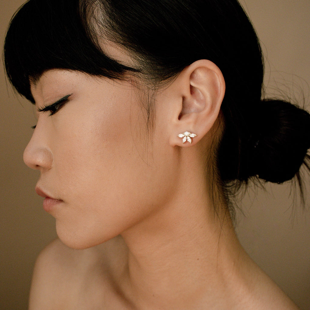Marquise diamond stud earrings set in 18K gold, worn on left ear with smooth, luminous skin and dark hair pulled back.