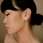 Marquise diamond stud earrings set in 18K gold, worn on left ear with smooth, luminous skin and dark hair pulled back.