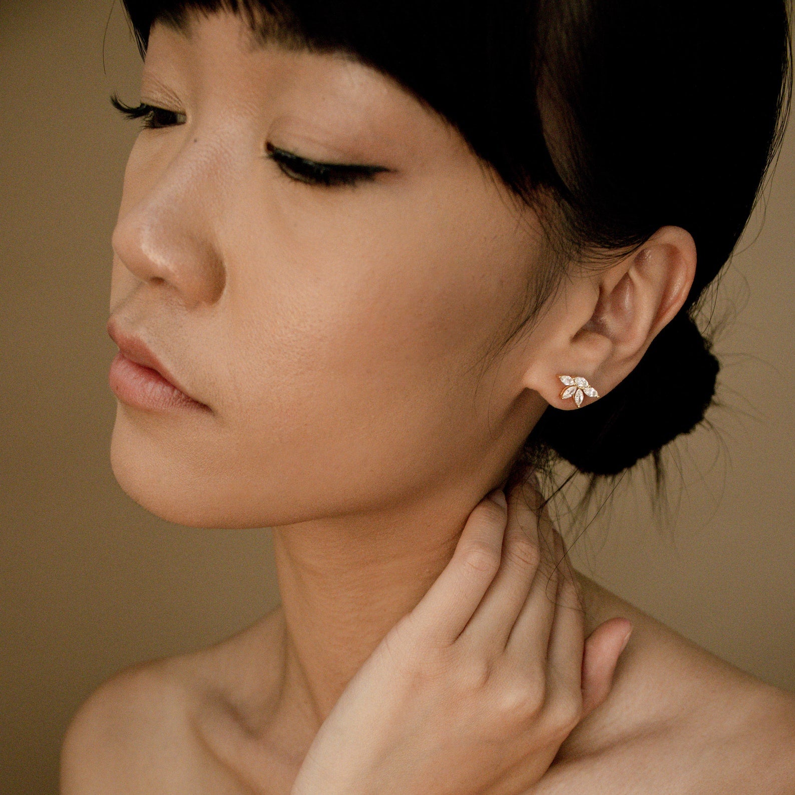 Woman wearing marquise diamond stud earrings set in 18K gold with pave detailing, close-up side profile against neutral.
