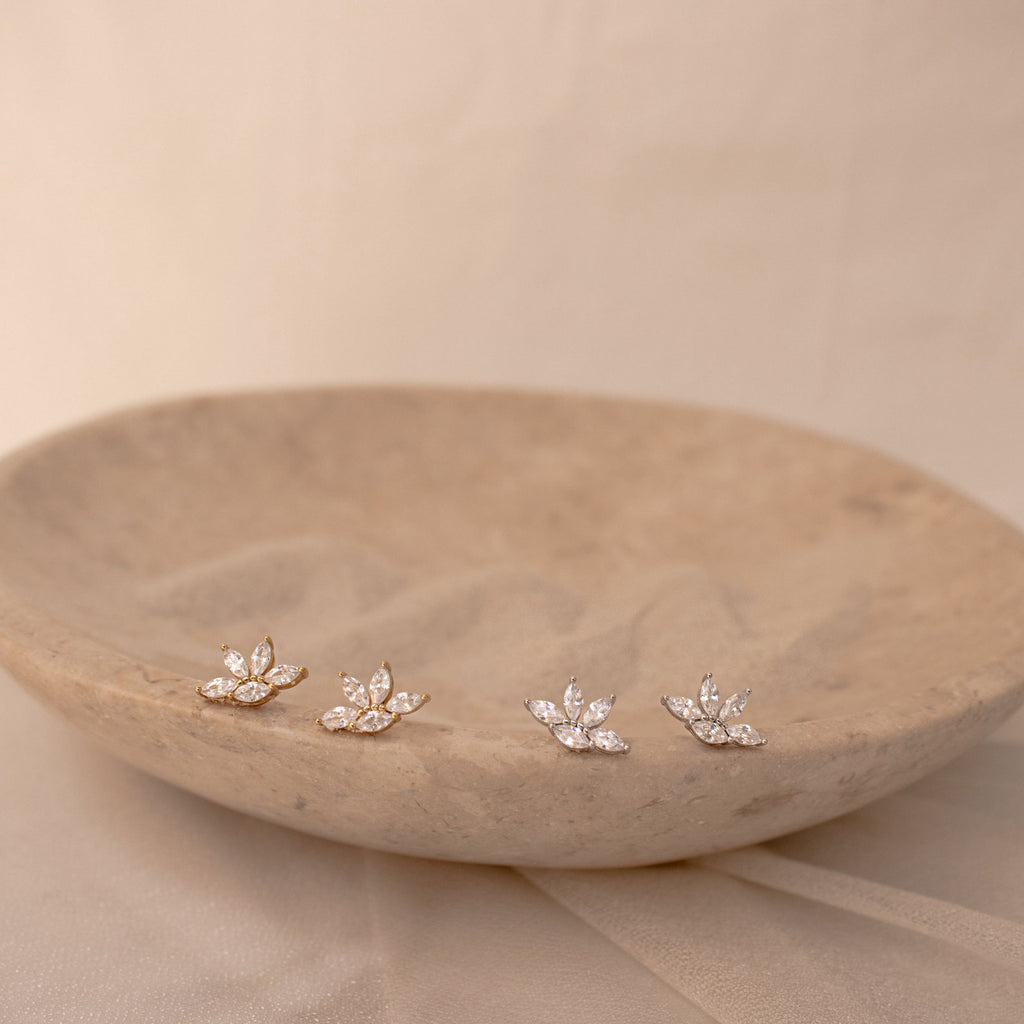 Marquise diamond stud earrings in 18K gold and sterling silver with pave-set diamonds, displayed on a beige stone dish with.