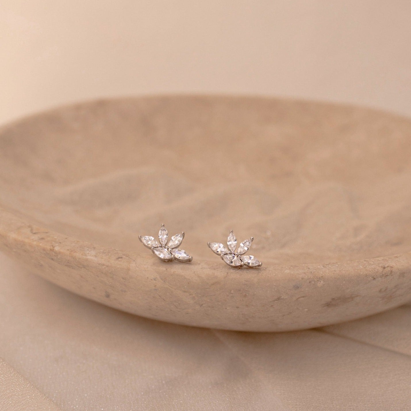 Marquise diamond stud earrings with clustered pear-shaped stones set in 18K gold, displayed on a carved beige stone dish.
