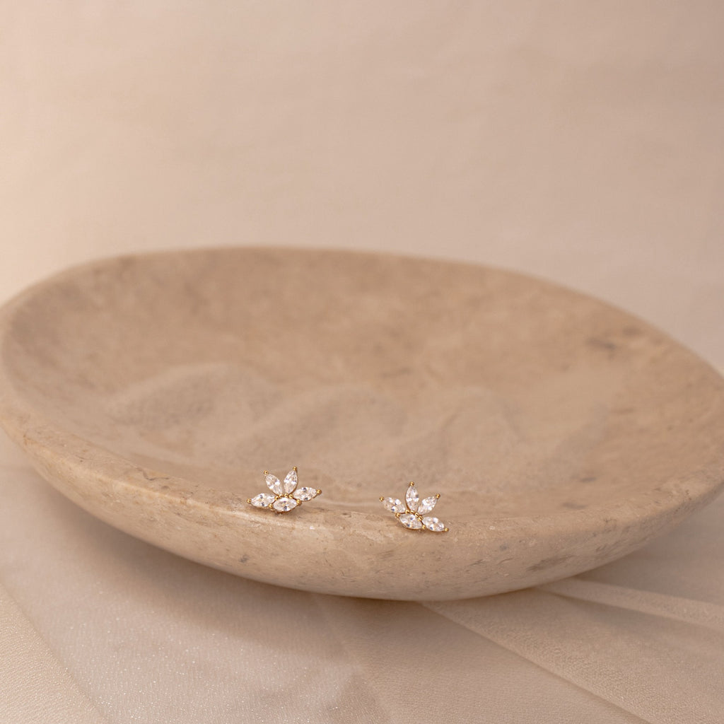 Marquise diamond stud earrings set in 18K gold, arranged in a delicate floral cluster on a textured beige dish.