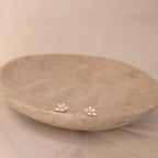 Marquise diamond stud earrings set in 18K gold, arranged in a delicate floral cluster on a textured beige dish.