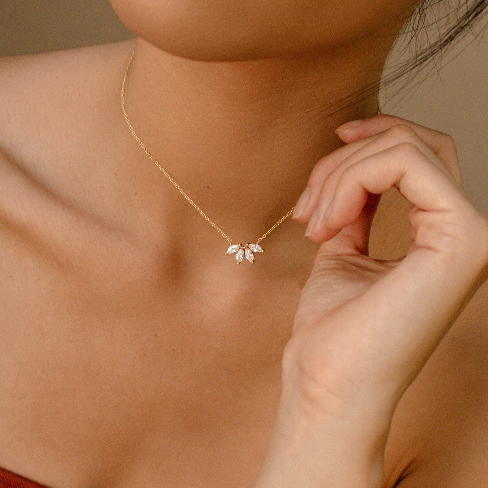 A close-up of a woman wearing a dainty gold necklace with marquise-cut stones shaped like a floral fan at the center of her collarbone.